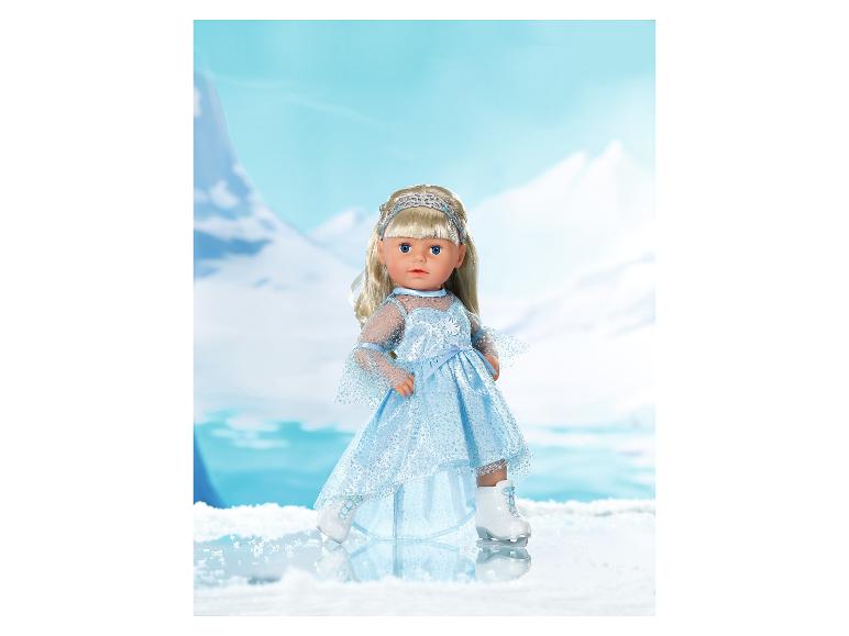 Pop in blauwe jurk en schaatsen, met een bergachtige winterachtergrond.