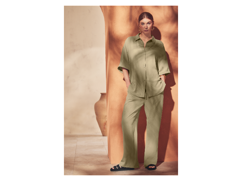 Een vrouw poseert in een lichtgroene jumpsuit en zwarte sandalen.