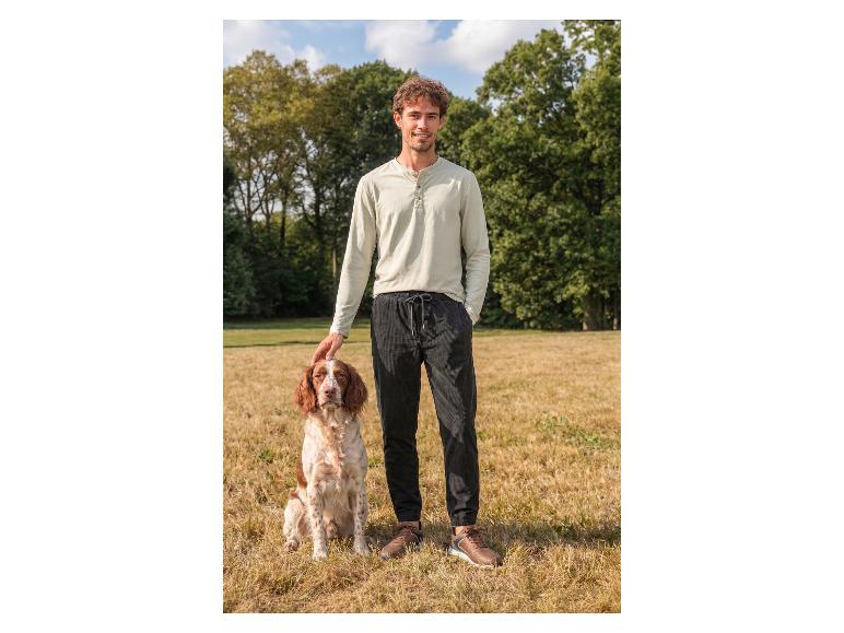 Man in shirt met lange mouwen en broek aait een hond buiten.