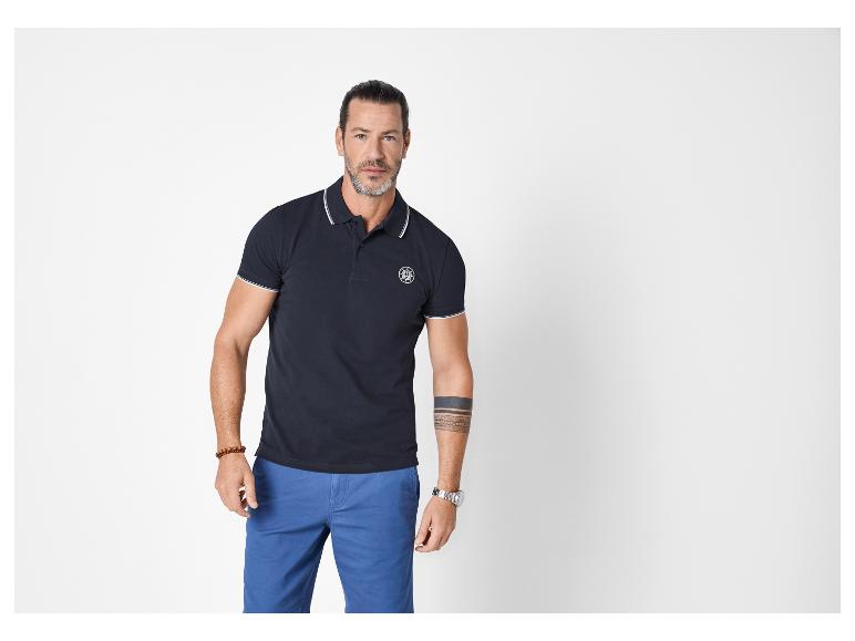 Man in een marineblauwe poloshirt met witte strepen en blauwe shorts.