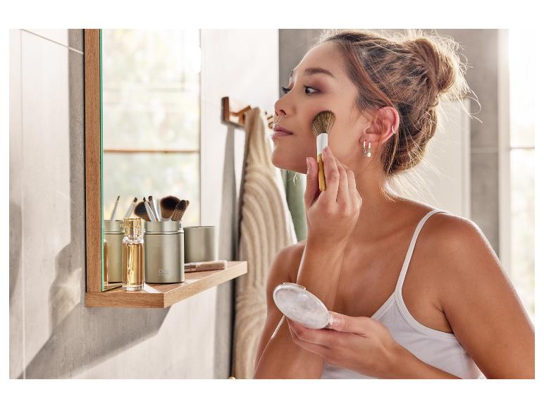 Een vrouw die make-up aanbrengt met een borstel en een poederdoos in een badkamer.