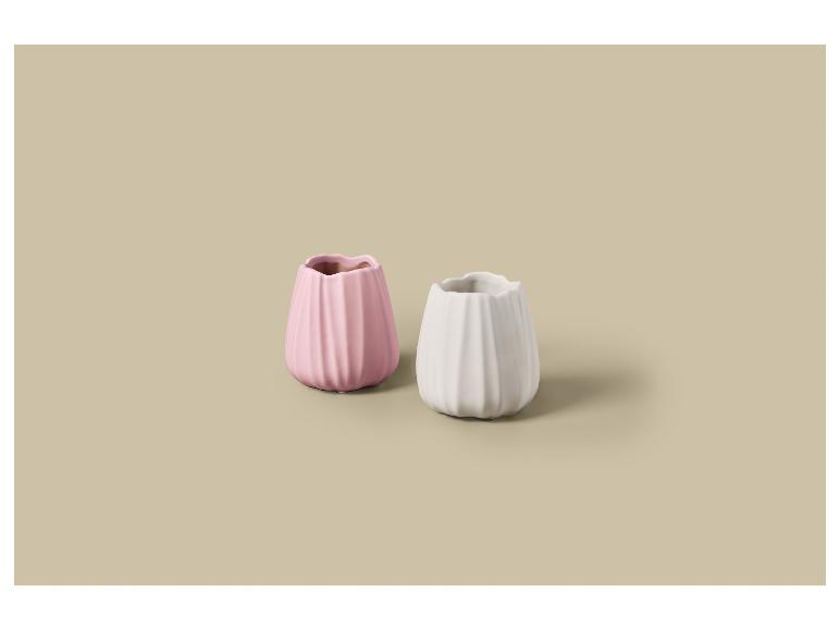 Twee kleine geribbelde vazen, één roze en één wit, op een beige achtergrond.