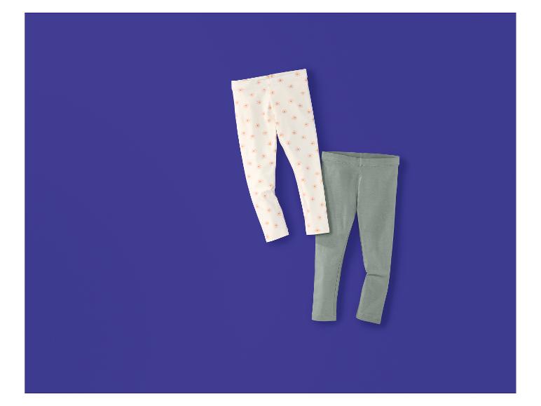 Twee kinderleggings: één wit met bloemenprint en één effen grijs.