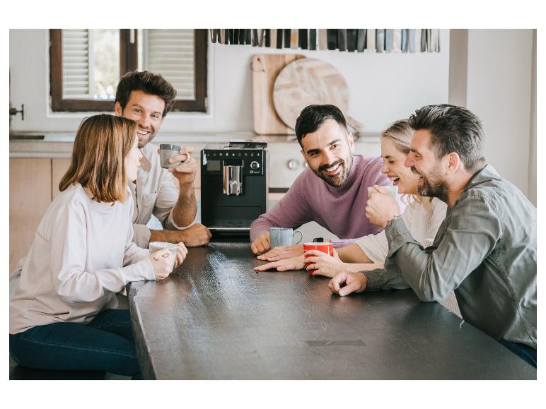 Vrienden genieten van koffie en een gesprek rond een tafel met een koffiezetapparaat.