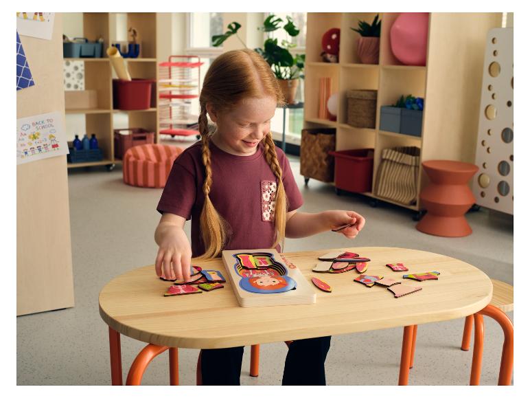 Een jong meisje speelt aan een tafel met een houten LUPILU® lichaamspuzzel.