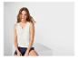 Vrouw in witte kanten top en denim shorts zit op een witte kubus.