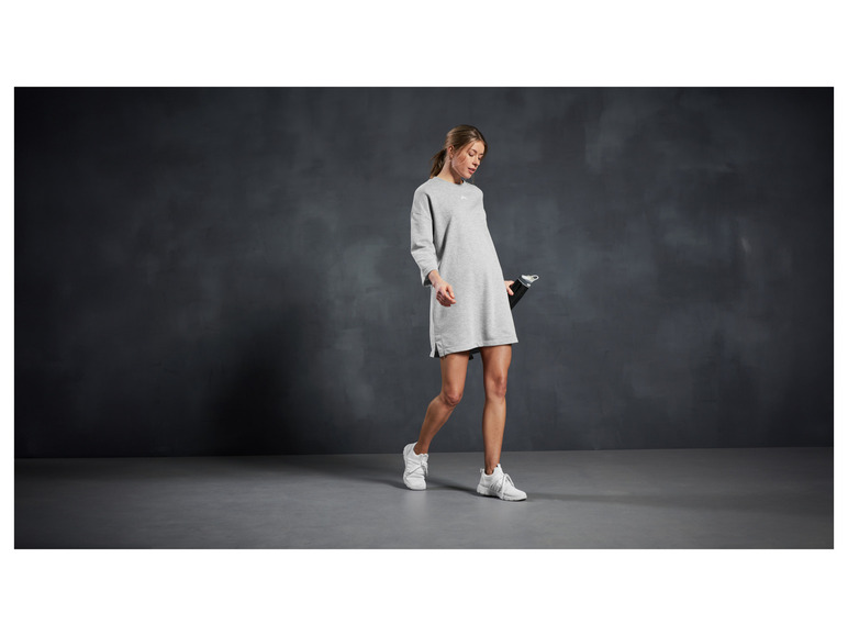 Een vrouw draagt een grijze trui en witte sneakers.