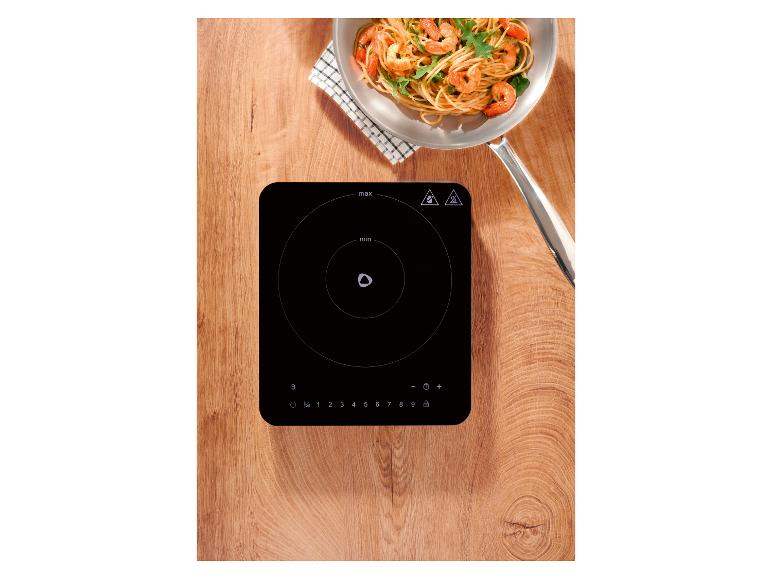 Inductiekookplaat met een pan garnalenpasta op een houten ondergrond.