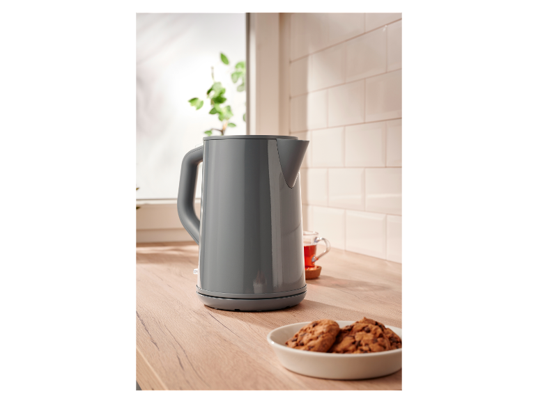 Een grijze waterkoker op een houten aanrecht naast koekjes.