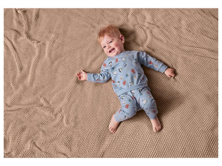 Baby in blauwe pyjama met pinguïns en beren op een bruine deken.