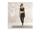 Een vrouw in zwarte leggings en sportbeha staat op een yogamat.