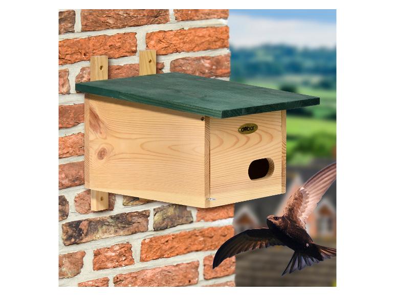 Houten vogelhuisje aan bakstenen muur met vliegende zwaluw.