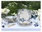 Buitentafel gedekt met wit en blauw servies, gouden bestek en bloemstukken.
