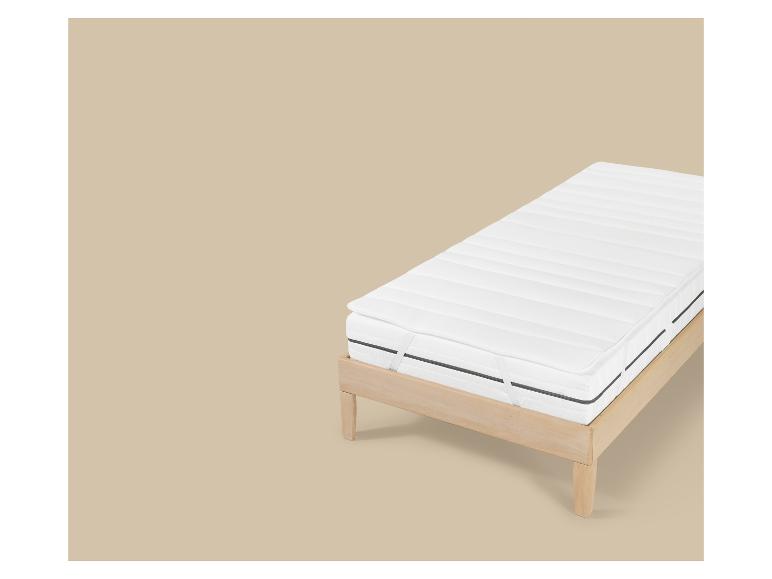 Wit matras met topper op een licht houten bedframe.