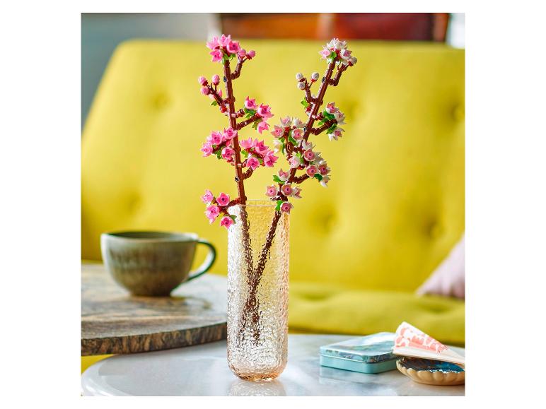 Vaas met Lego Botanicals kersenbloesems op een tafel, met een kopje en blik op de achtergrond.