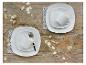 Twee gedekte tafels met wit vierkant servies, kopjes en schotels op een houten tafel met decoratieve takken.