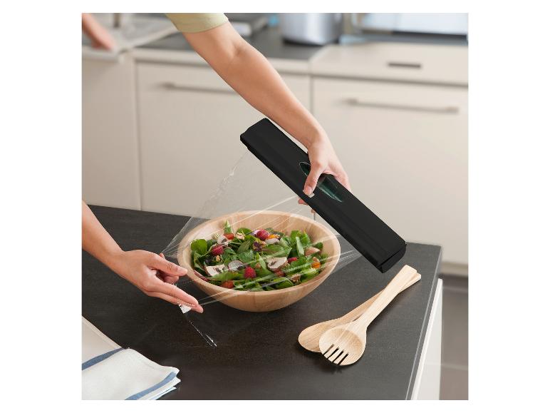 Een vrouw gebruikt een zwarte huishoudfoliehouder in de keuken om een salade te bedekken.