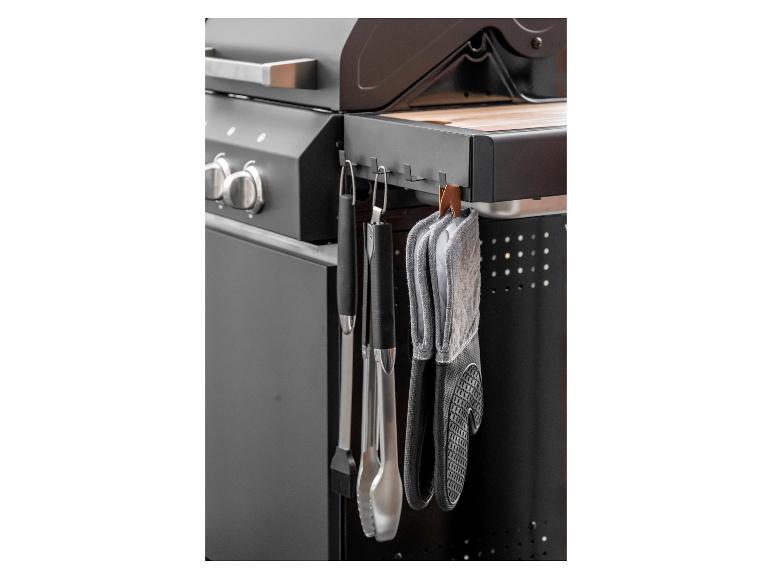 Grillhandschoenen en grillgereedschap hangen aan een zwarte barbecue.