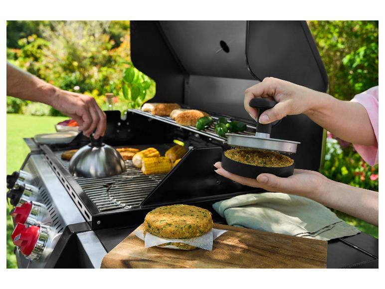 Twee handen bereiden burgers en maïs op een buitengrill.