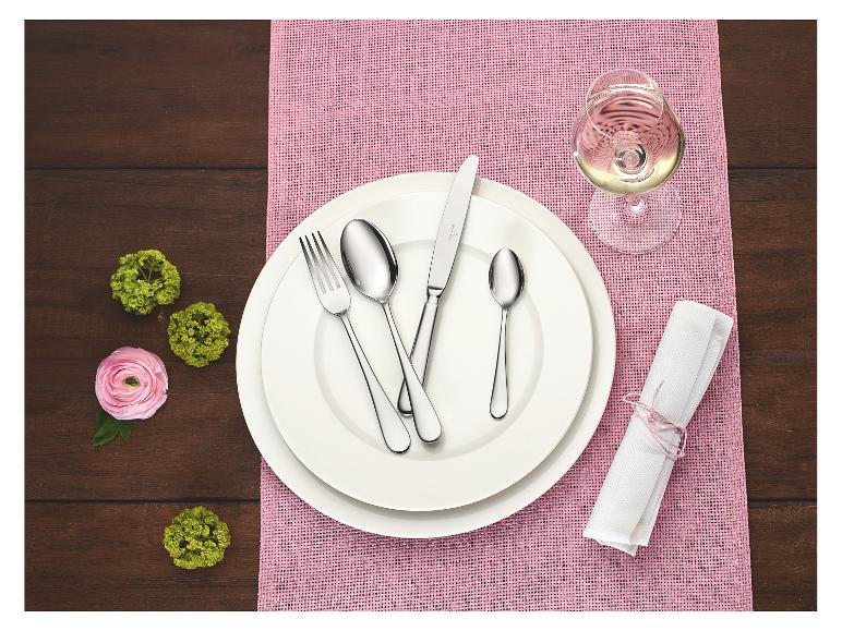Elegante tafeldekking met witte borden, bestek, een glas witte wijn en roze accenten.