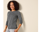 Lachende vrouw in een shirt met lange mouwen en jeans, leunend tegen een muur.