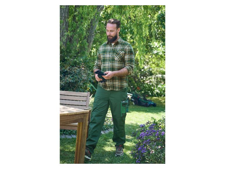 Een man in een geruite trui en groene werkbroek met tuinhandschoenen.