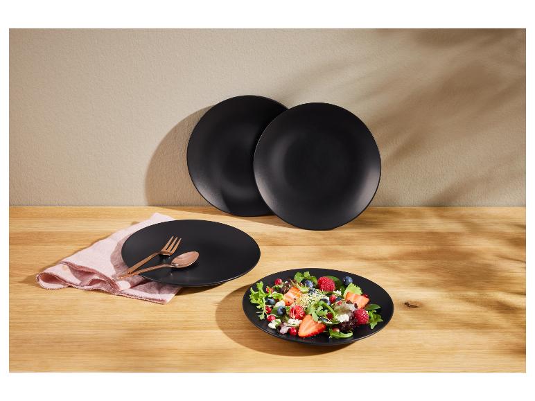 Elegante zwarte borden met salade en gouden bestek op een houten tafel.