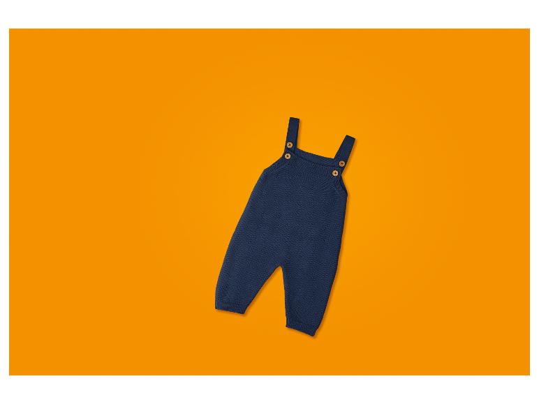 Donkerblauwe gebreide baby romper met bretels en houten knopen, op een oranje achtergrond.