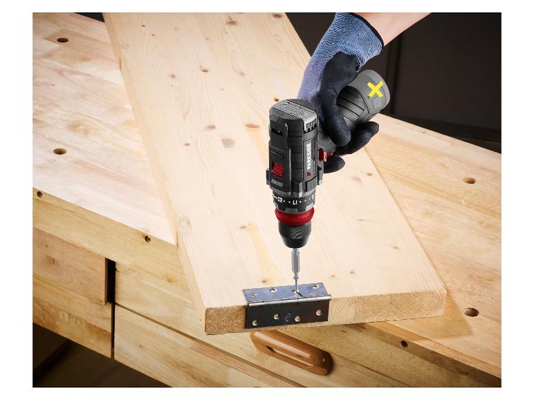 Persoon met handschoen schroeft scharnier in hout met accuboormachine.