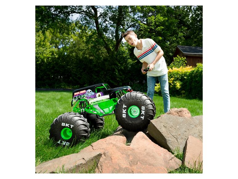 Een jongen bestuurt een Grave Digger RC monstertruck op gras, met rotsen op de voorgrond.