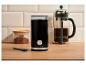 Zwarte elektrische koffiemolen, cafetière en pot gemalen koffie op een houten aanrecht.