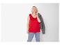 Vrouw in rood mouwloos shirt en jeans, met grijze jas over haar schouder.