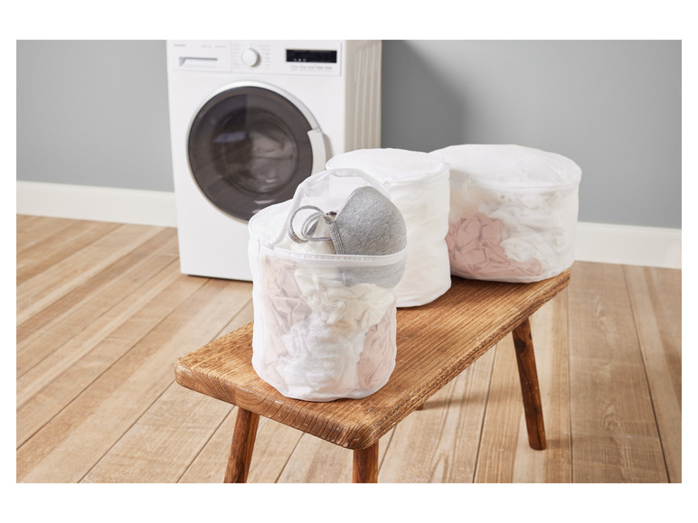 Drie waszakken op een houten bankje naast een wasmachine.