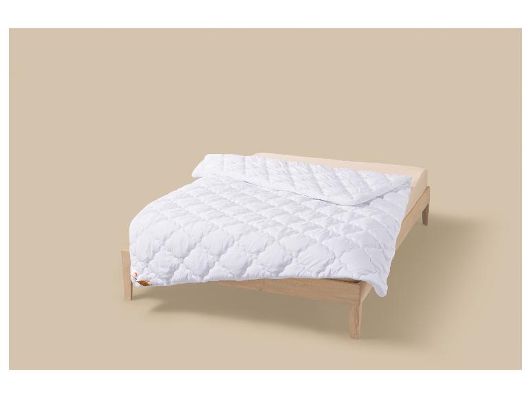 Wit gewatteerd dekbed op een houten bed.