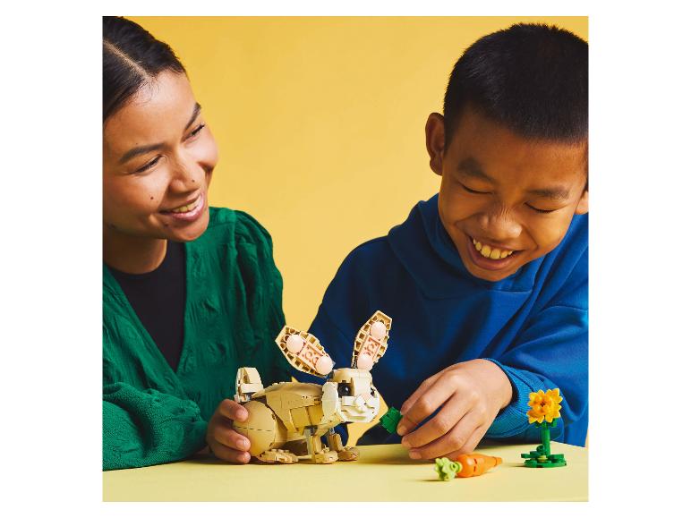 Een vrouw en een kind spelen met een LEGO-konijn en wortels.