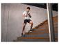 Man in sportkleding rent trap op, draagt grijs t-shirt en zwarte shorts.
