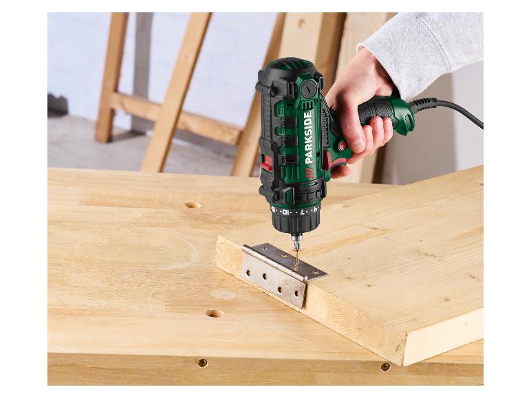 Groen-zwarte elektrische boor-/schroefmachine bevestigt een metalen scharnier aan een houten plank.