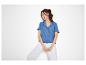 Vrouw in blauw overhemd met korte mouwen en witte broek, lachend.