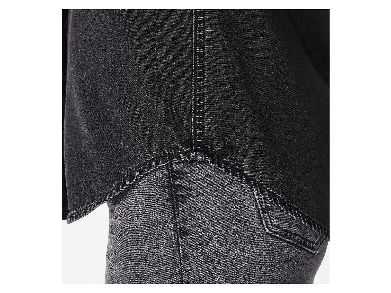Detail van een zwart jeans overhemd over een donkere jeans.