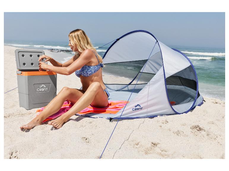 Vrouw op strand opent koelbox naast strandtent.