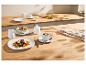 Elegant wit servies met vlees en linzen, salade en koffie op een houten tafel.