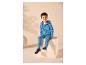 Jongen in blauwe hoodie-jumpsuit en sneakers, zittend op een witte kubus.