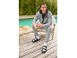 Man in grijs trainingspak en zwarte sandalen met witte sokken, lachend met een groene smoothie.