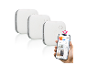 Drie witte rookmelders met een smart home-app op een smartphone.