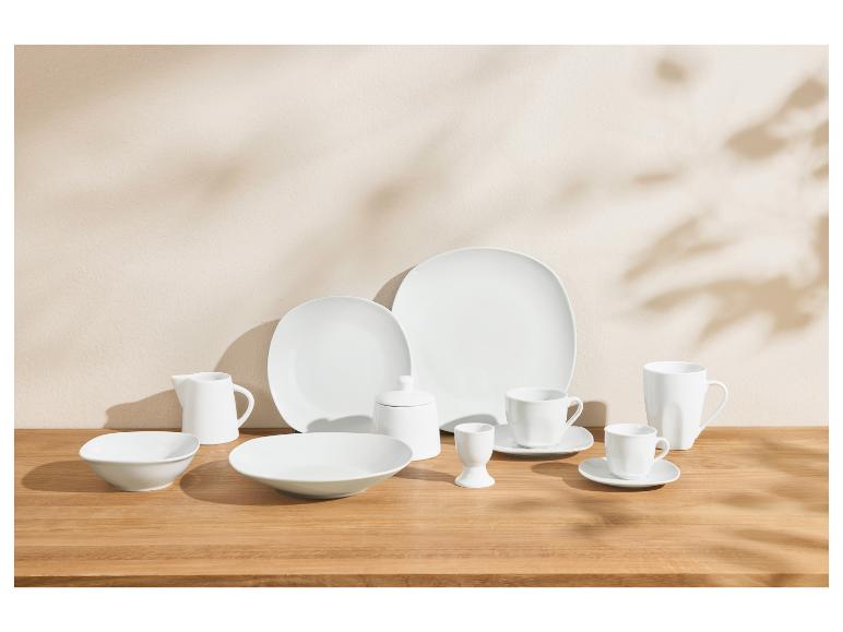 Wit porseleinen servies met borden, kommen, kopjes en serveerstukken op een houten tafel.