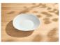 Lege witte kom op een lichte houten tafel met bladschaduwen.