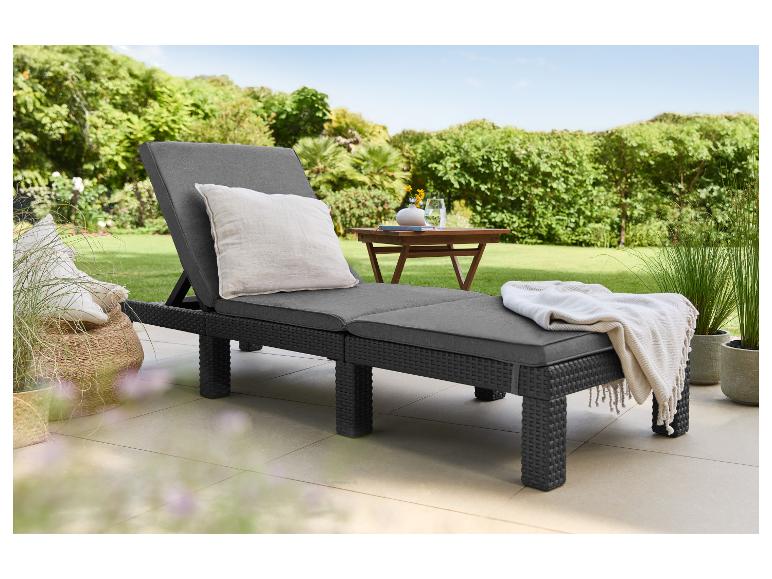 Donkergrijze ligstoel met kussens en deken op een terras met tuin op de achtergrond.