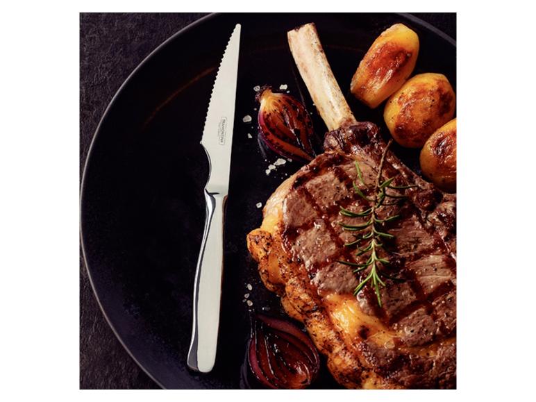 Steak met bot, geroosterde aardappelen, uien en rozemarijn op een zwart bord, met een mes.