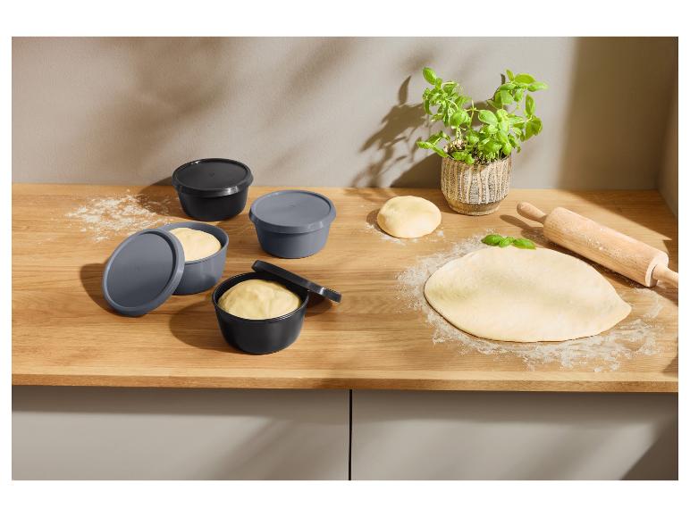 Deegbakjes met deksels, uitgerold deeg met bloem en een houten deegroller op een houten aanrecht.