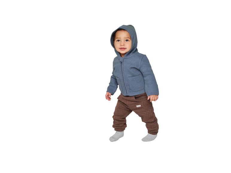 Peuter in een blauwe hoodie en bruine gewatteerde broek.